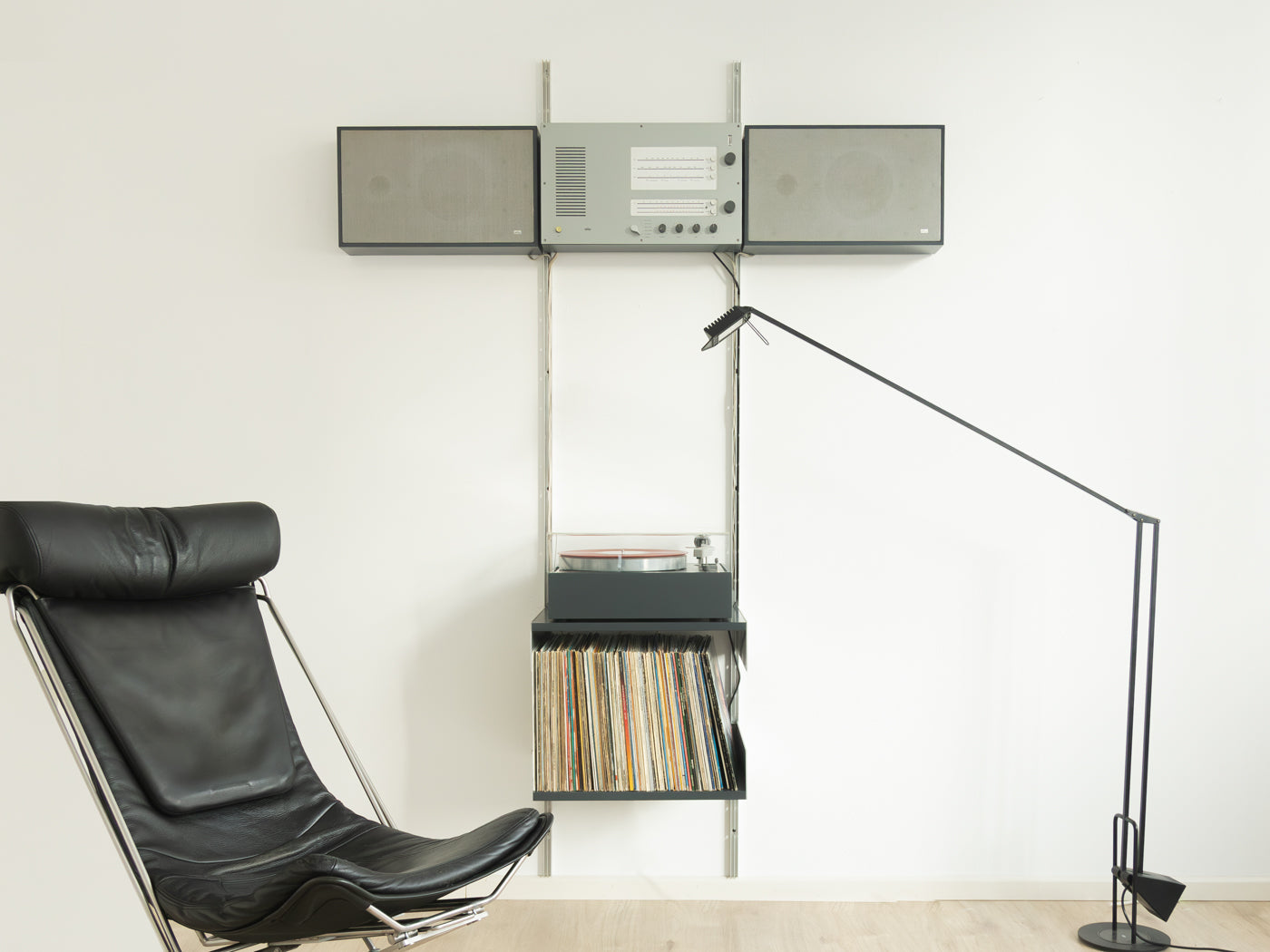 Braun TS45 Wandanlage von Dieter Rams mit Lautsprechern, Radio, Verstärker und Plattenspieler an weißer Wand neben schwarzem Ledersessel und Stehlampe